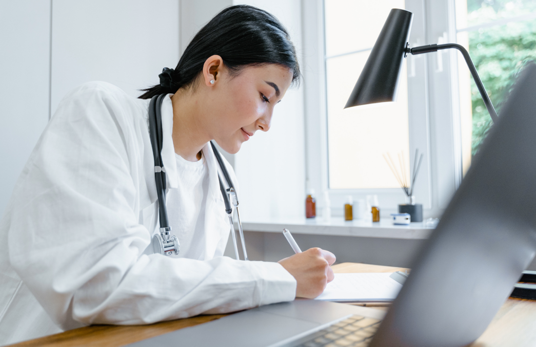 woman taking notes on a notepad in front of laptop