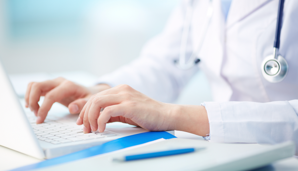 On The Blog: 4 Ways your EHR can help improve clinical efficiency. Photograph of a doctor using a laptop to enter charting data.