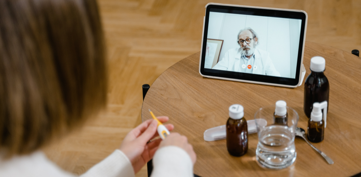 doctor on an ipad talking to a patient holding a thermometer and pill bottles on a table